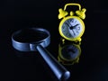 A yellow clock and magnifying glass with reflection on a black background. Royalty Free Stock Photo