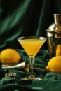 Yellow cocktail in martini glass with lemons and bar tools on dark green satin fabric Royalty Free Stock Photo