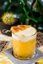 Yellow cocktail with white protein foam in a beautiful old fashion glass, decorated with a mango skewer