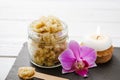 Yellow color handmade sugar body scrub in glass jar. Burning candle and pink orchid blossom for decoration on white studio backgro