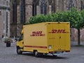 Yellow colored delivery van of carrier DHL with red company logo parking on Domfreihof square in the center of Trier.