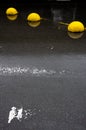 Three yellow concrete hemispheres with reflection on the wet asphalt.