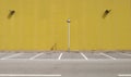 Yellow concrete wall with a streetlight in the middle. Sidewalk and asphalt road with parking in front.