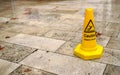 Yellow cone with caution slippery surface sign, on wet pavement tiles.