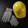 Yellow construction hard hat and light gray work gloves on a smooth black surface. Royalty Free Stock Photo