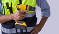 A yellow cordless electric drill with battery in the hand of a construction worker wearing an green reflective safety vest. Close