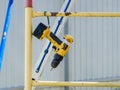 A yellow cordless screwdriver hangs on a scaffold bar