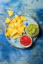 Yellow corn nachos chips with guacamole dip and tomato salsa over blue plate on blue stone background Royalty Free Stock Photo