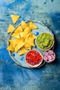 Yellow corn nachos chips with guacamole dip, tomato salsa and radishes over blue plate on blue background.