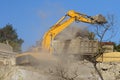 Yellow crawler excavator demolishes dilapidated real estate for future construction of modern house