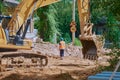 Yellow crawler excavator at a road reconstruction site in a village with old log houses. Summer sunny day. Royalty Free Stock Photo