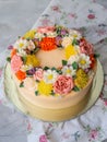 Yellow cream cake decorated with buttercream flowers - peonies, roses, chrysanthemums, carnations - on white wooden background. Royalty Free Stock Photo