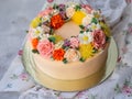 Yellow cream cake decorated with buttercream flowers - peonies, roses, chrysanthemums, carnations - on white wooden background. Royalty Free Stock Photo