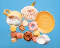 A yellow cup with coffee, donuts, macaroons, peony and hand holding milk cream jug flying over a blue background Royalty Free Stock Photo