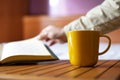 Yellow cup of coffee and a man turning a page in a book Royalty Free Stock Photo
