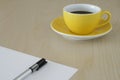 Yellow cup of coffee and a pen on paper