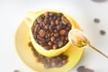 Yellow cup full of natural coffee beans, top view, on a white background. Selective focus. Morning coffee. Royalty Free Stock Photo