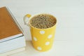 Yellow cup of hot black coffee with fresh bubble in heart shape on book stack decorated with pencil and vintage key on white