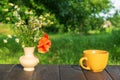 Yellow cup of hot coffee or tea and a bouquet of flowers on a wooden table in a green garden in the morning or evening. Summer Royalty Free Stock Photo