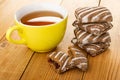 Yellow cup with tea, broken gingerbread with jam, whole gingerbreads on wooden table