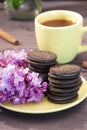 Yellow cup of tea with chocolate biscuits with a sprig of lilac and cinnamon