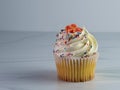 Yellow cupcake with white frosting, an orange fondant flower and lots of sprinkles sitting on a sandstone surface with a white Royalty Free Stock Photo