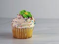 Yellow cupcake with white swirled frosting coated in sprinkles and topped with a green fondant flower as a decoration, sitting on