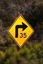 Yellow curved sign with an advisory speed against a blurred background