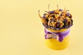 Yellow cylindrical box with a lilac bow filled with dried fruits on a yellow background, copy space