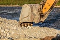 Yellow digger excavator machine bucket digging in stones ground by the river