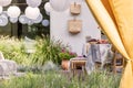 Yellow drapes and white lanterns in the garden with fruits on table, flowers and bags. Real photo