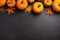 Yellow dried leaves and small orange pumpkins on black background, top view, copy space. Halloween, Thanksgiving holiday concept