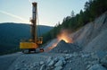 Yellow drilling machine bores holes in granite rock on blasting site. Construction of new road in mountain area, rock exploding Royalty Free Stock Photo