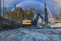 Yellow drilling machine under colorful rainbow in sky stands on granite rock and drills holes for new road construction. Wide Royalty Free Stock Photo