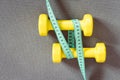 Yellow dumbbells and green measuring tape on grey fitness mat.