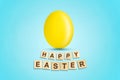 Yellow easter egg on a blue background. Happy Easter, word written on wood blocks. Background