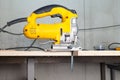 A yellow electric jigsaw ready for use stands in a sawn wood building material on a workbench in a workshop for carpentry work. Royalty Free Stock Photo