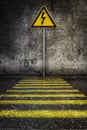 Yellow electricity warning sign at grunge wall in front of pedestrian crossing Royalty Free Stock Photo