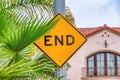 Yellow End sign and green palm tree leaves against sky and house with balcony Royalty Free Stock Photo