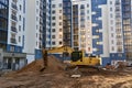 Yellow excavator  in action at a construction site on the background of the facade of a modern multi-storey building. Tall house Royalty Free Stock Photo