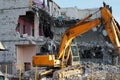 Yellow excavator demolishing a multi-storey building. Destroyed floors of the building, are pieces of stone, concrete, fittings.
