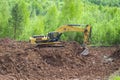 He yellow excavator digs red clay with a large bucket. Clay mining