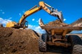 Yellow excavator loading soil into a dumper truck Royalty Free Stock Photo