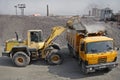 Yellow excavator loads gravel into orange dumper truck tipper. Royalty Free Stock Photo
