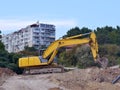 Yellow excavator at the site of the road construction works near the residential building