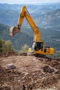 A yellow excavator works in the mountains. Construction of roads
