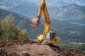 A yellow excavator works in the mountains. Construction of roads