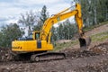 A yellow excavator works in the mountains. Construction of roads