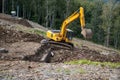 A yellow excavator works in the mountains. Construction of roads