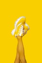 Yellow female sneakers on long woman legs isolated on yellow background. Vertical banner Royalty Free Stock Photo